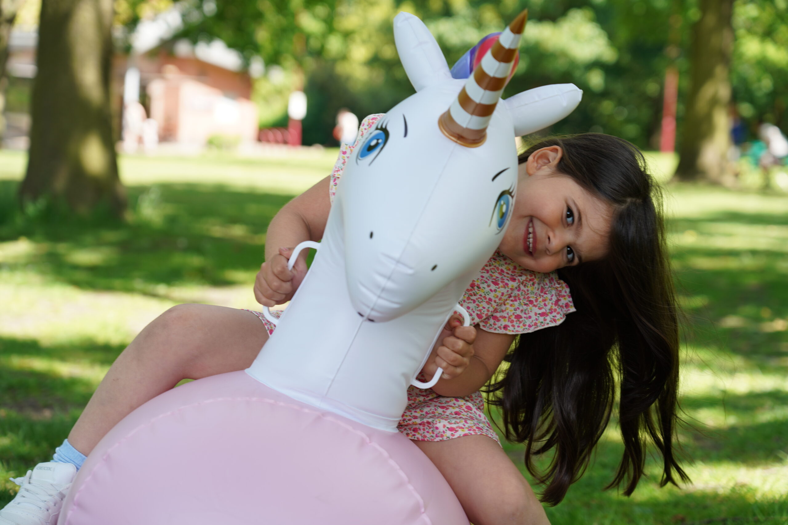 Young girl playing on an inflatable unicorn hopper during a family photoshoot in the park