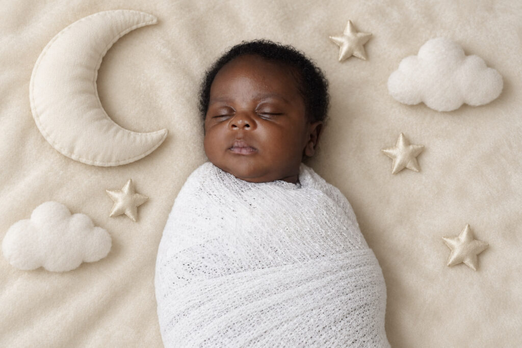 Sleepy newborn baby wrapped in a white swaddle with moon and star props during a newborn photography session