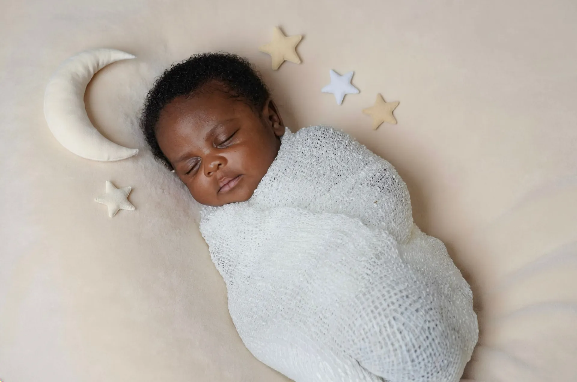 Sleepy newborn baby lying swaddled beside a crescent moon prop during a newborn photography session